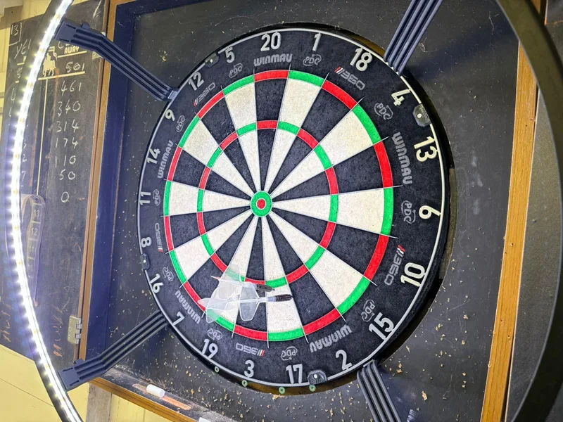 A dartboard in a cabinet with the old chalk scoreboard beside it