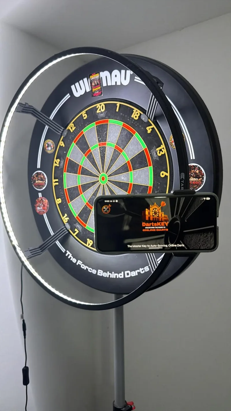 A phone clamped to the right side of a dartboard surround with a light ring