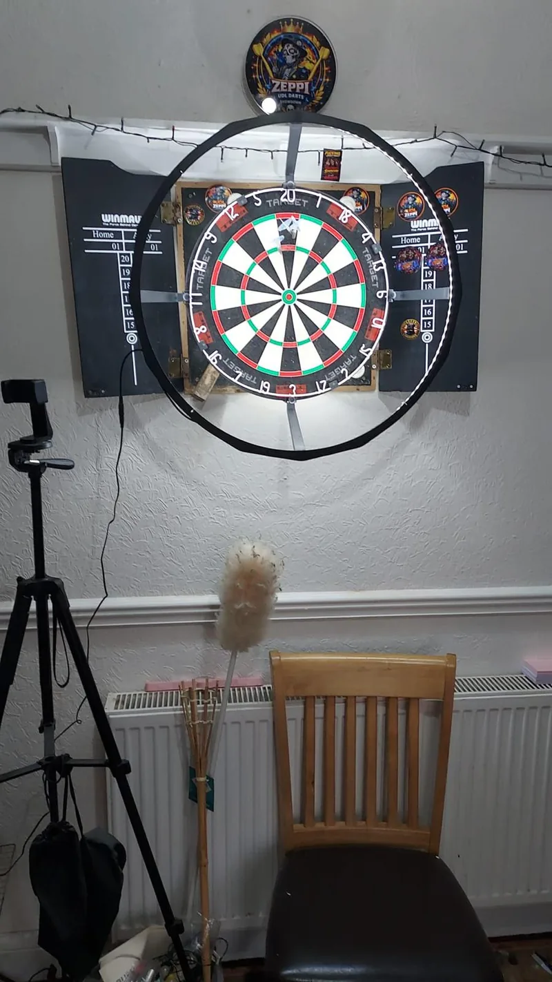 A phone on a tripod in front of a dartboard cabinet with a light ring