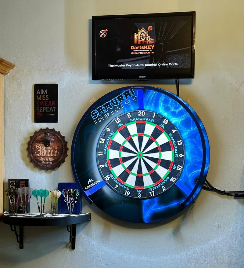 A blue-surround dartboard with DartsKEY's start screen on a TV above it